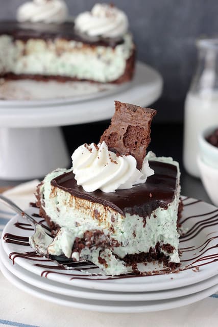 Close-up of a slice of Brownie Brittle Grasshopper Pie on a plate with a swirl of whipped cream and a piece of Brownie Brittle on top