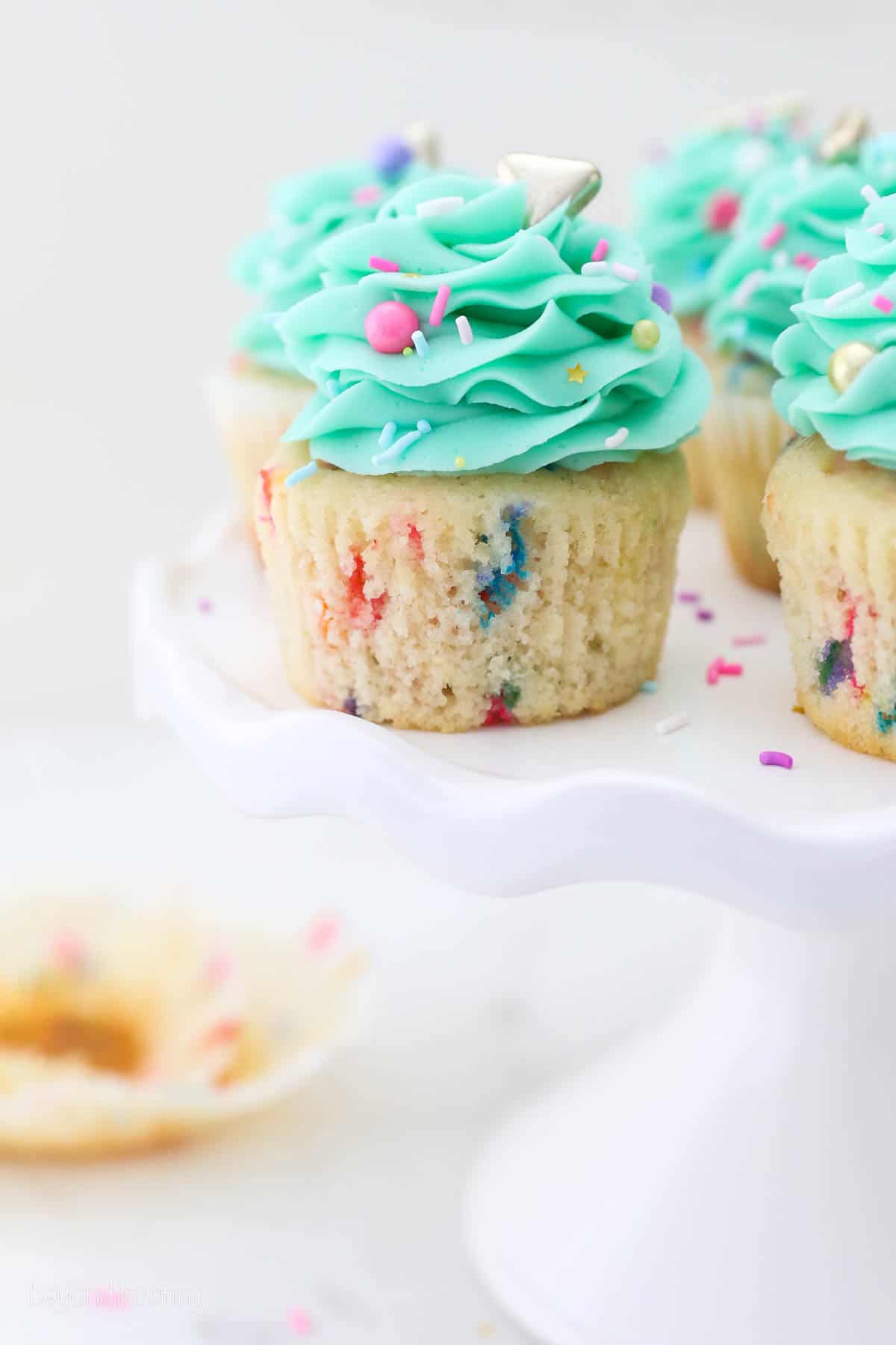 Funfetti cupcakes frosted with teal buttercream swirls and sprinkles on a white cake stand.