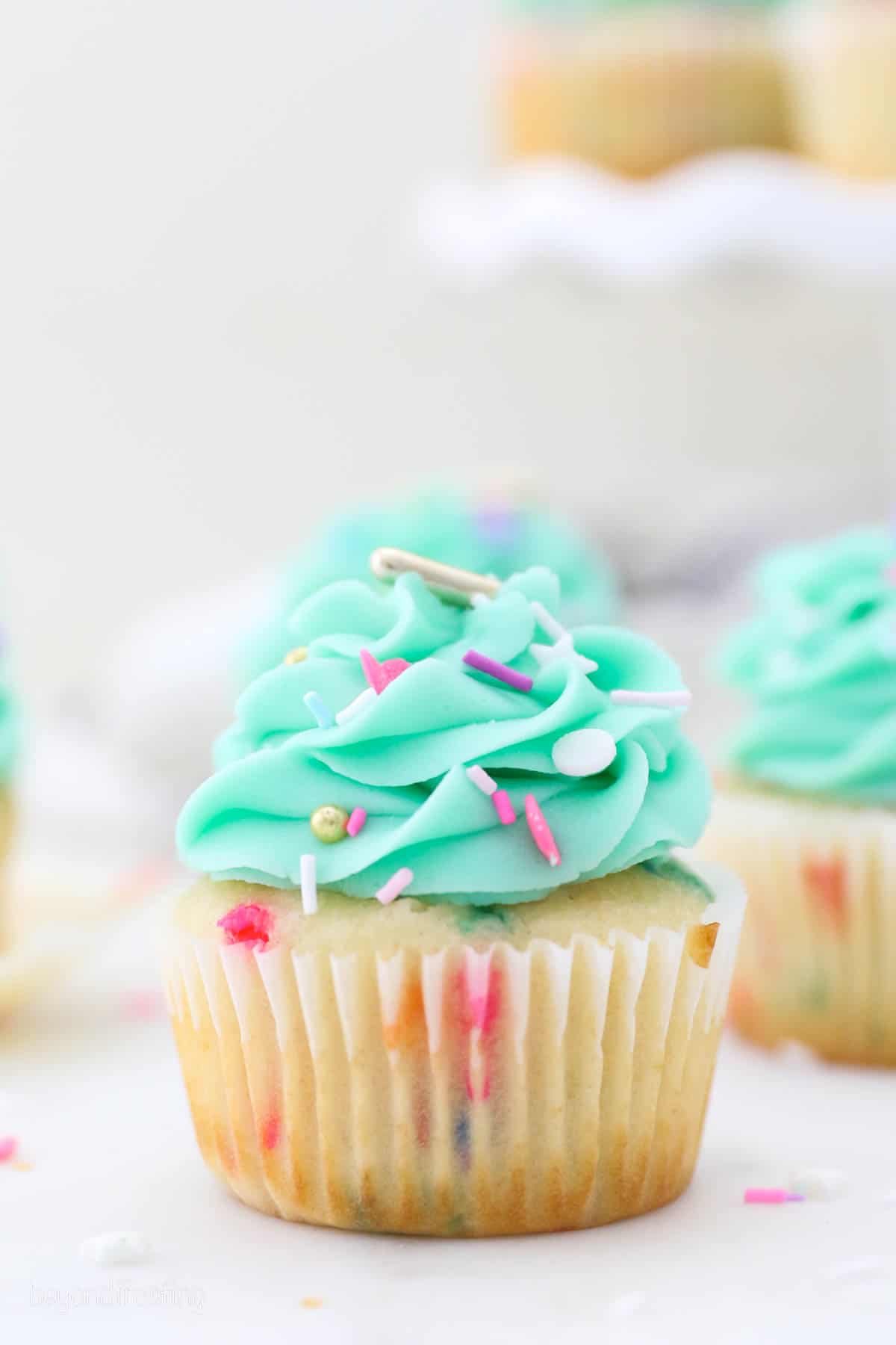 Close up of a funfetti cupcake frosted with a teal buttercream swirl and sprinkles.