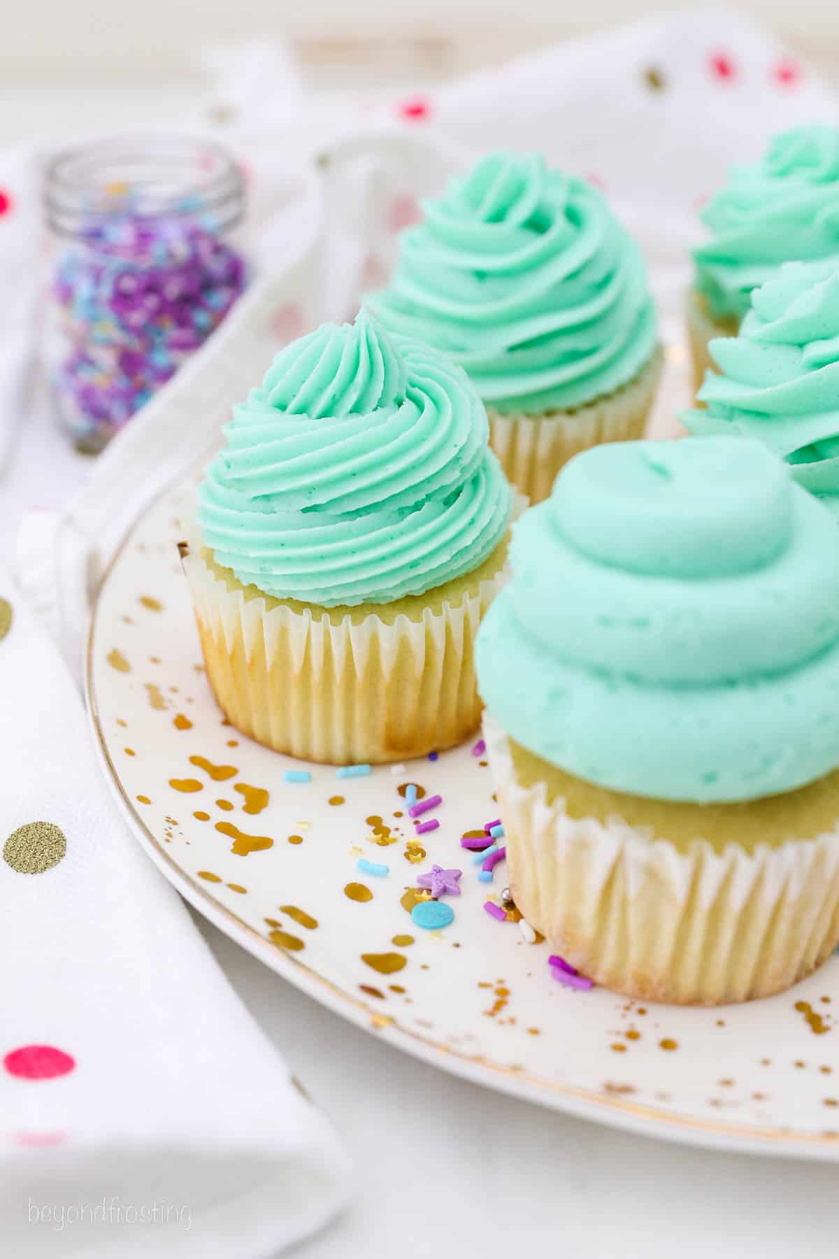 Vanilla cupcakes topped with swirls of teal frosting, piped with various piping tips on a plate.