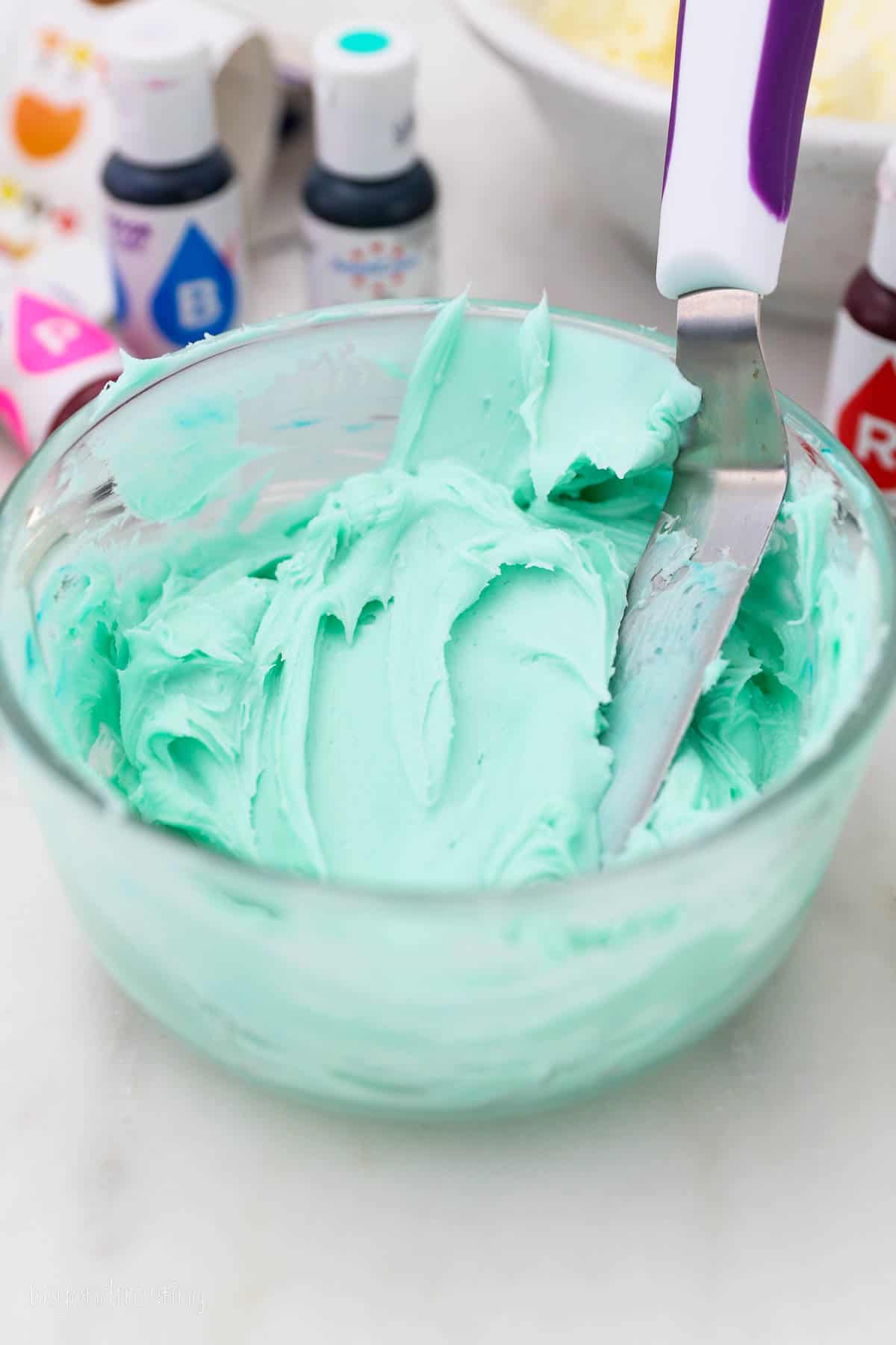 A bowl of teal colored vanilla buttercream with an offset spatula.