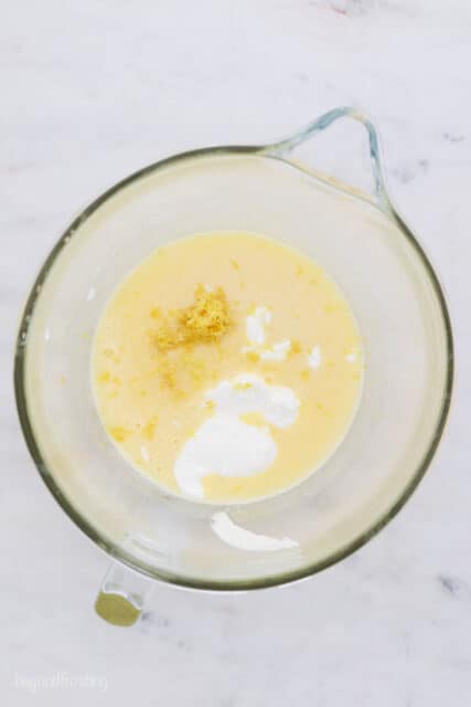 These lemon cupcakes are made with buttermilk and filled with bright citrus flavor, from the fluffy crumb to the creamy lemon frosting on top. Wet cupcake batter ingredients combined in a glass mixing bowl with a spout.