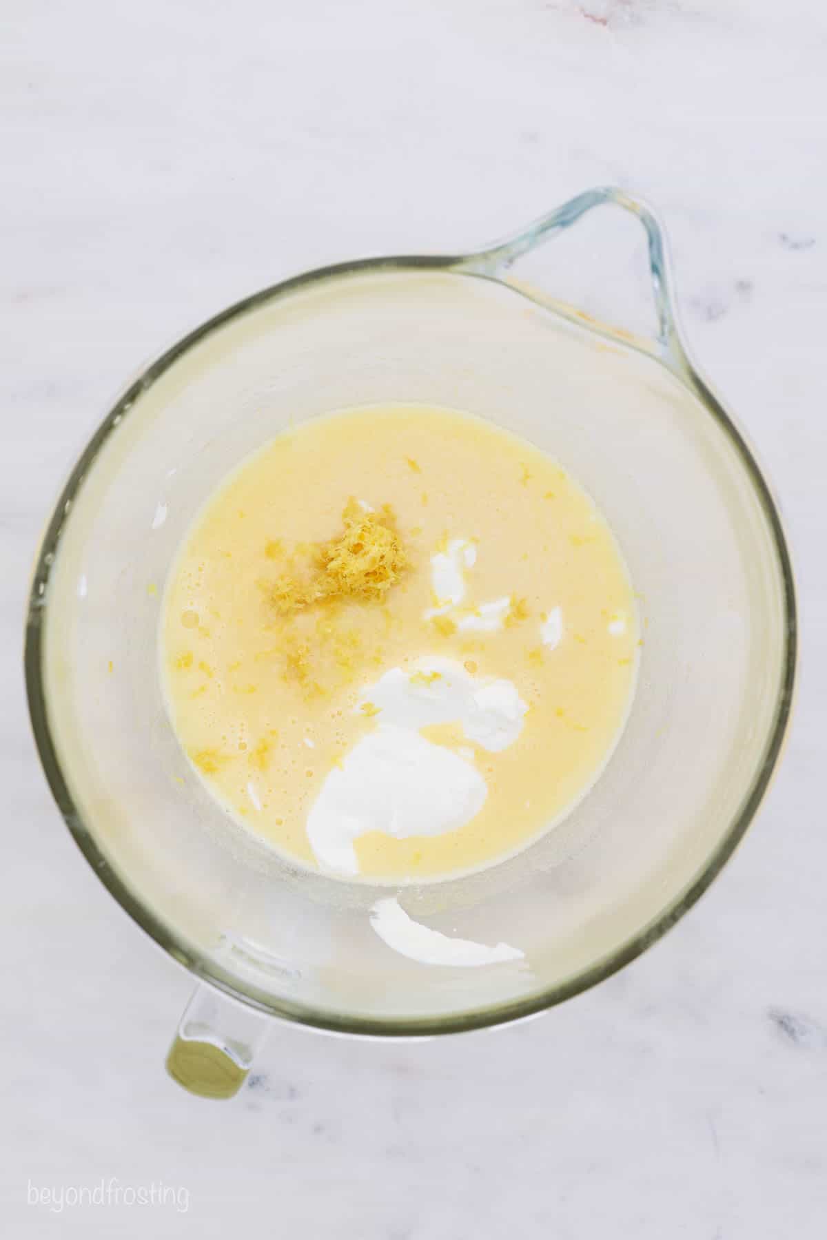 Wet cupcake batter ingredients combined in a glass mixing bowl with a spout.