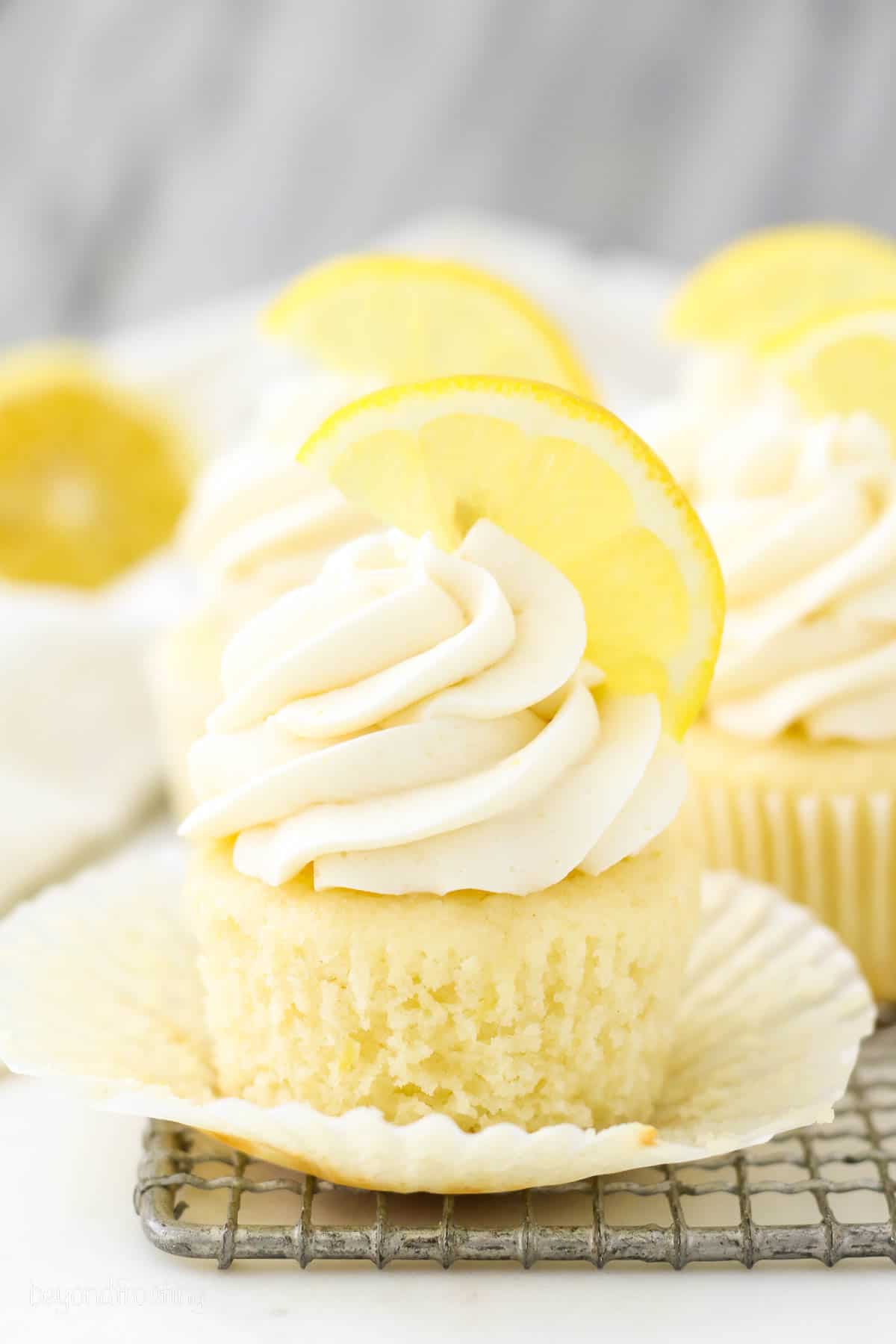 A partially unwrapped frosted lemon cupcake topped with half of a lemon wedge.