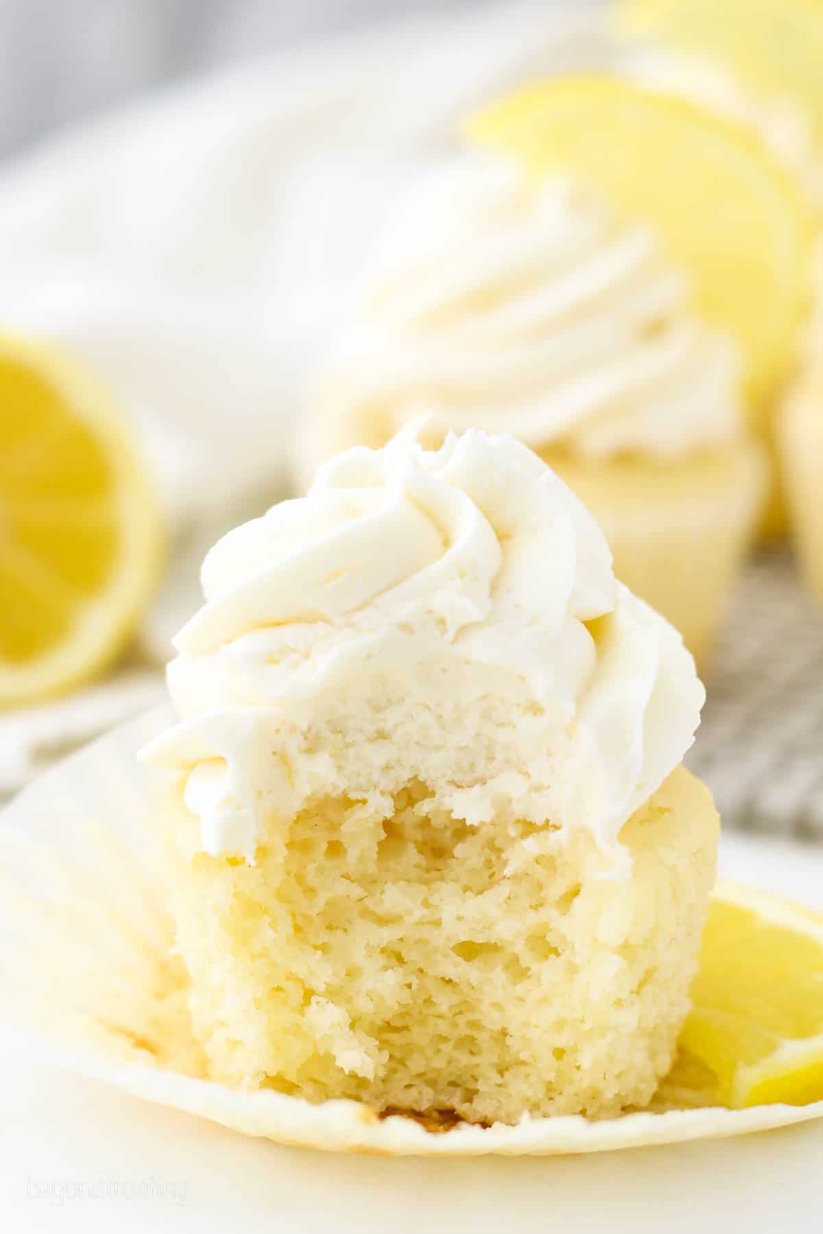 An unwrapped frosted lemon cupcake with a bite missing.