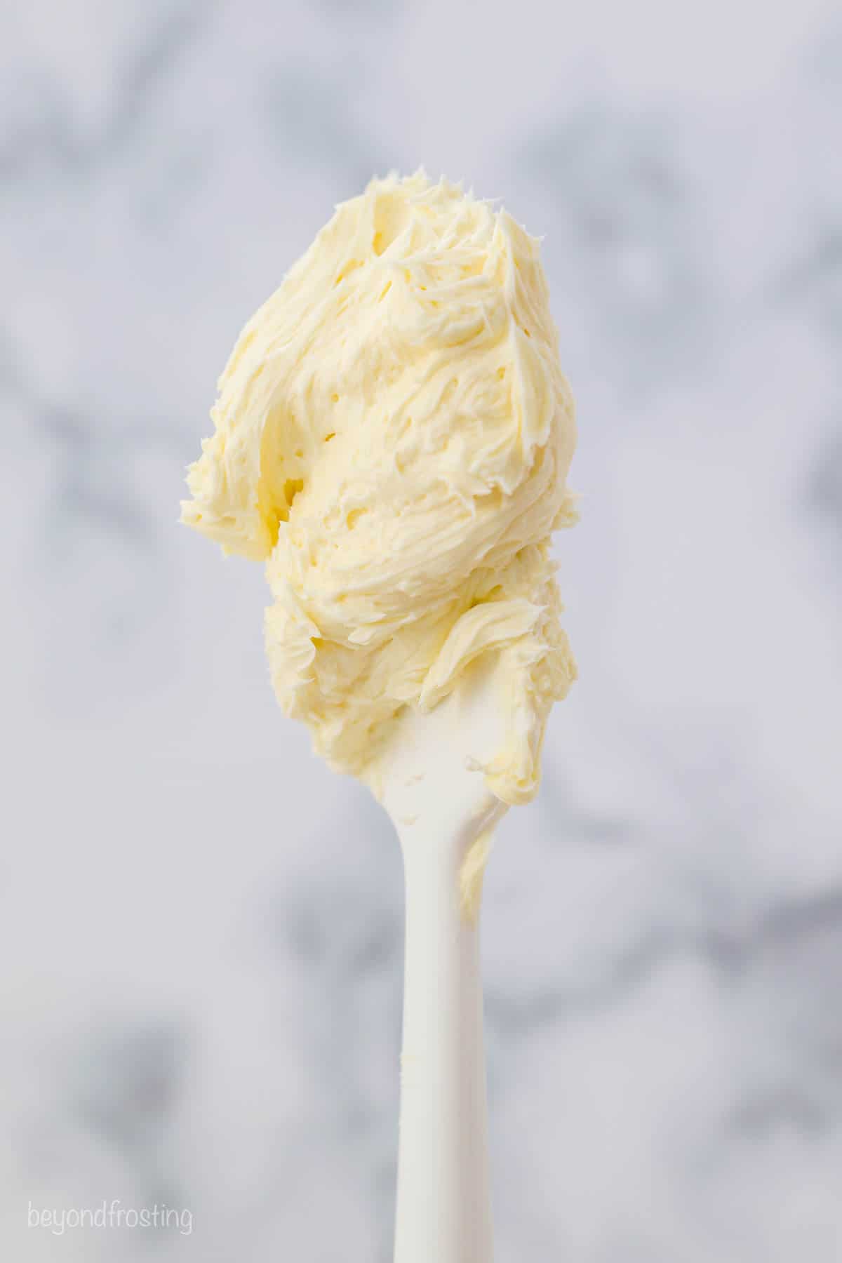 A white spatula with vanilla buttercream on it.