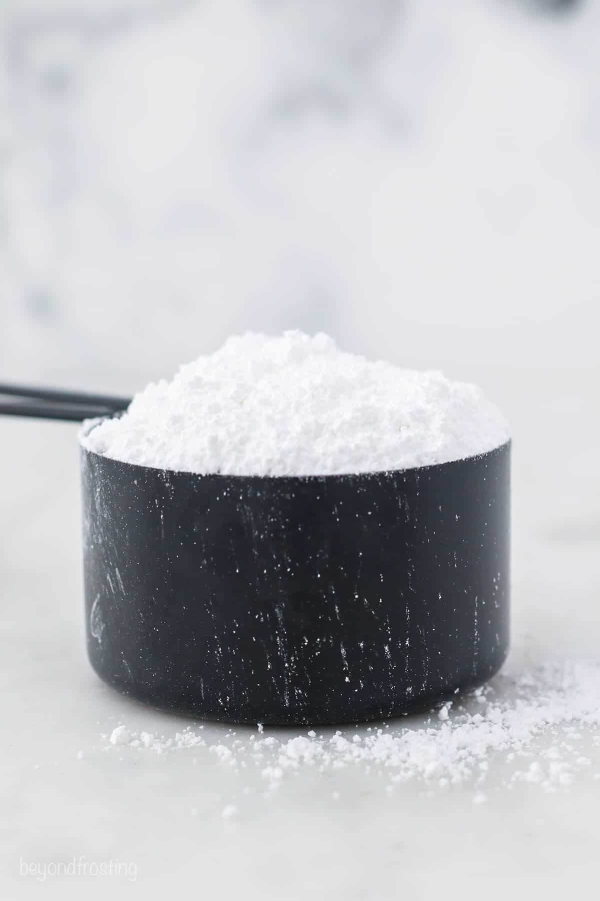 A black measuring cup filled with powdered sugar.