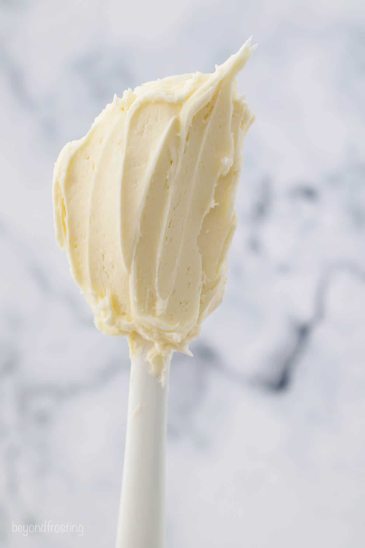 A white spatula with smoothed vanilla buttercream on it.