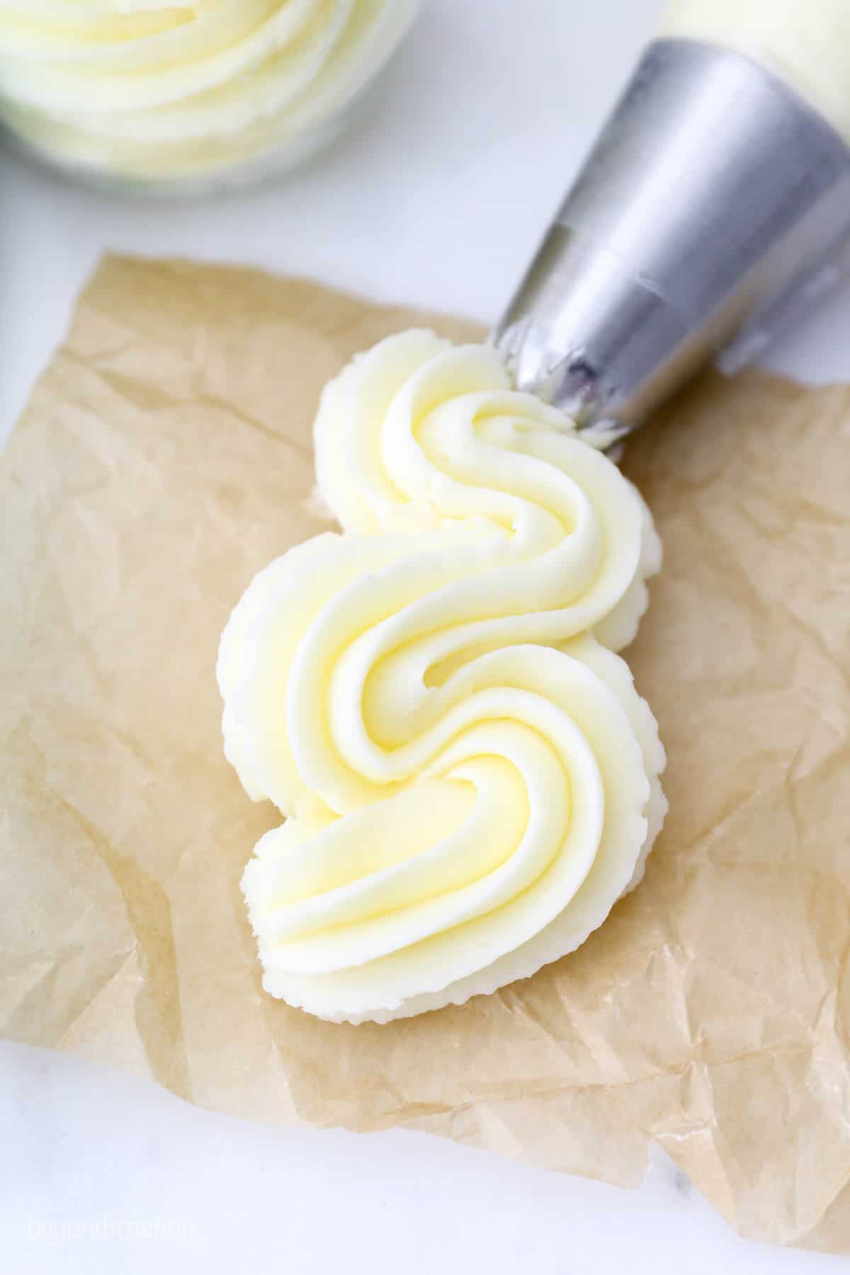 A big swirl of vanilla frosting piped onto a crumpled piece of brown parchment paper.