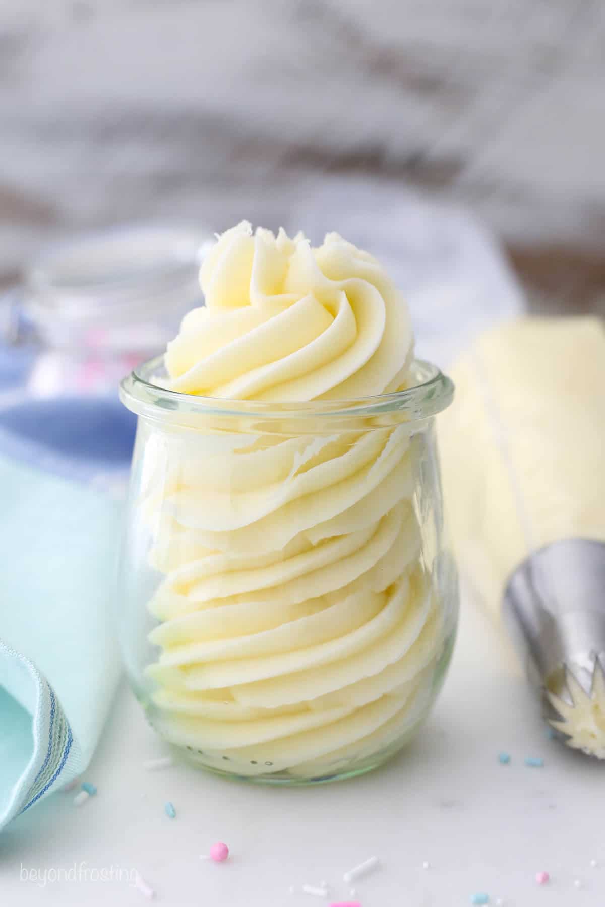 A small jar of piped vanilla buttercream next to a full piping bag.