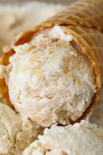 Close up of an apple ice cream cone resting in a tub of apple ice cream.