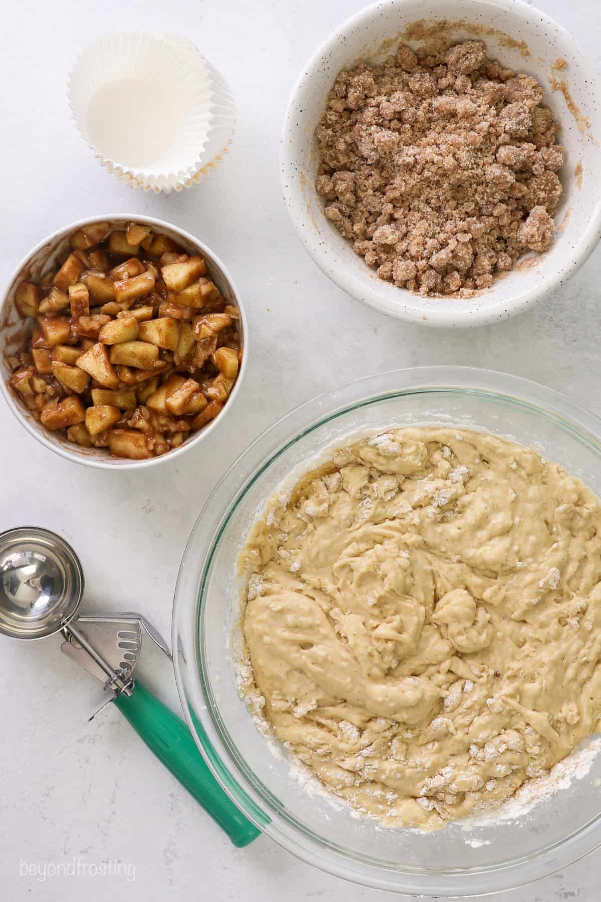 Overhead view of bowls of apple pie filling, streusel, and muffin batter next to an ice cream scoop.