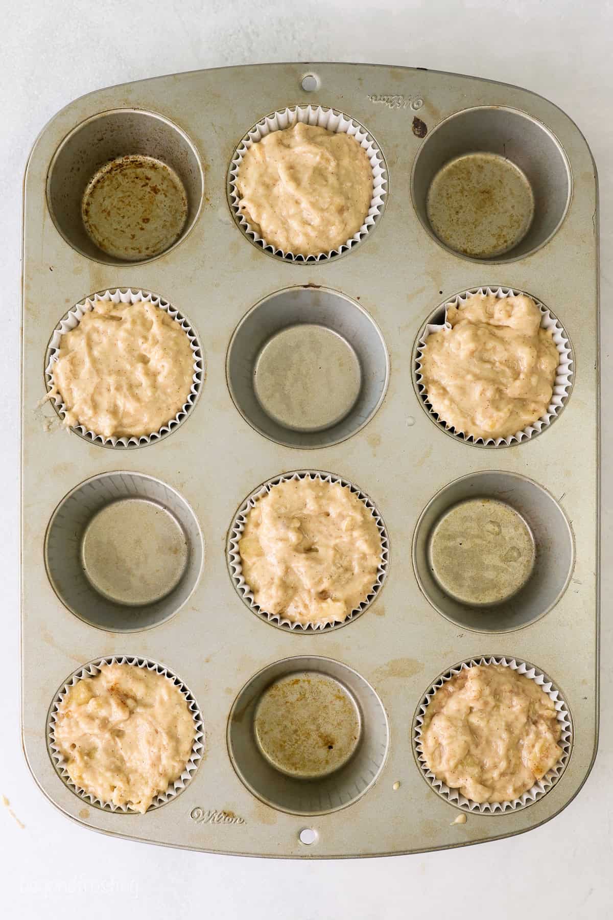 Overhead view of a muffin tin where every other well is filled with apple muffin batter.