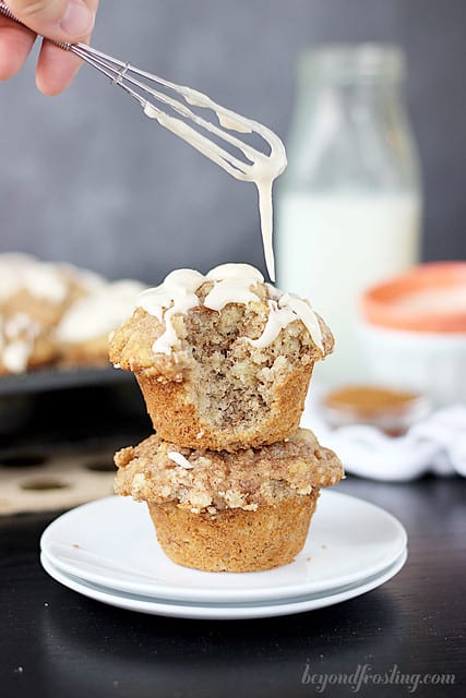 Frosting being drizzled over two cinnamon roll muffins on a plate