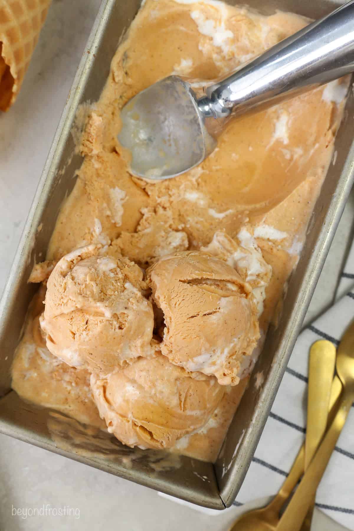 Overhead view of sweet potato ice cream in a loaf pan with an ice cream scoop.