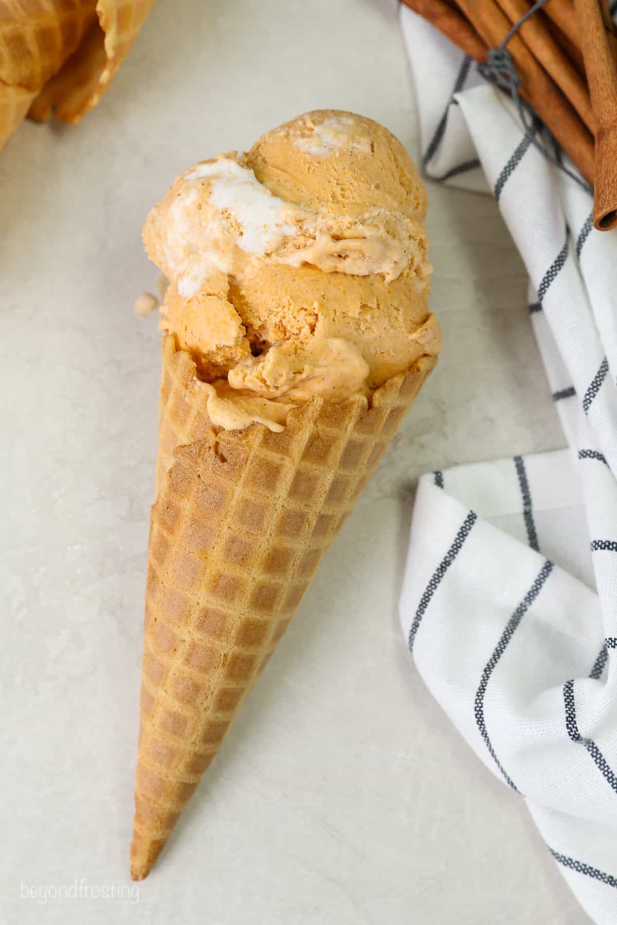 Overhead view of an ice cream cone with sweet potato ice cream laying on its side next to a striped tea towel.