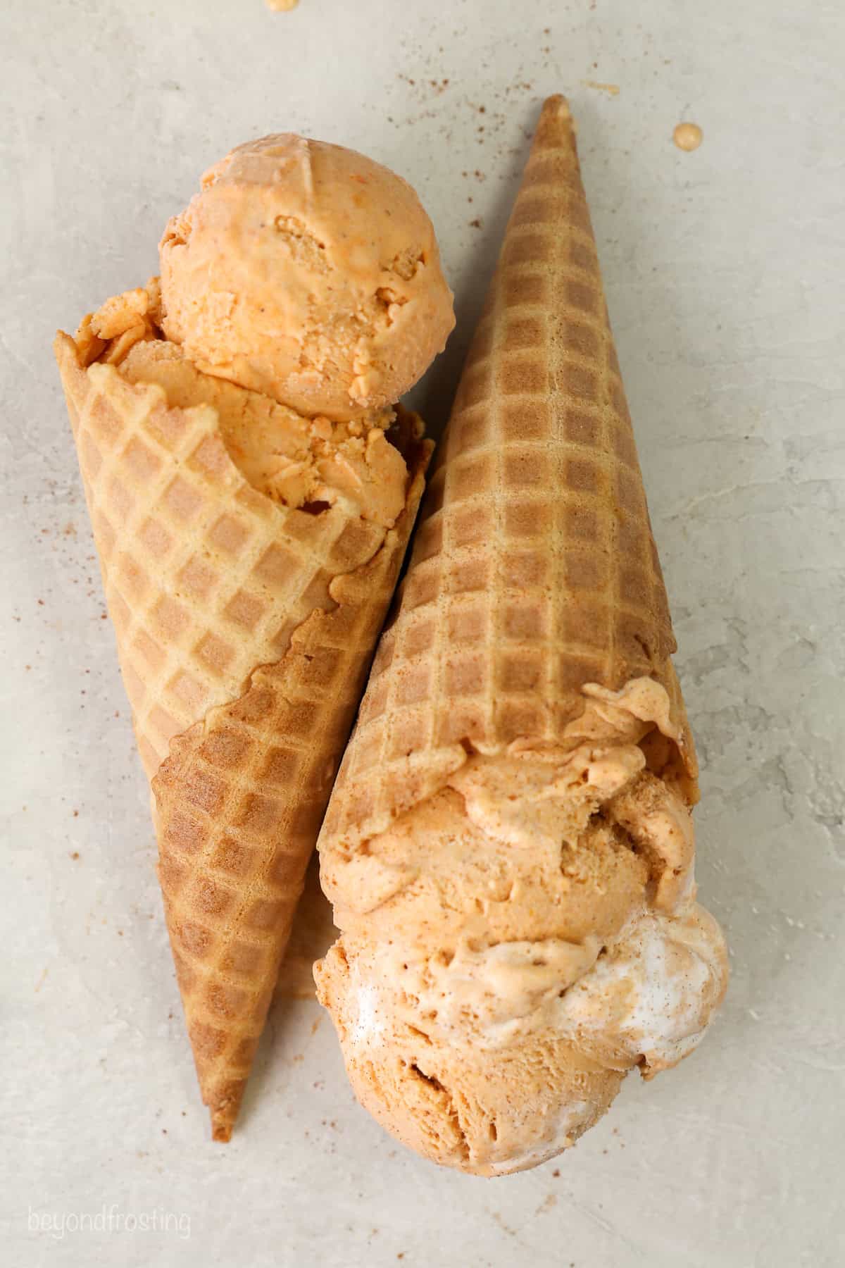 Overhead view of two ice cream cones with scoops of sweet potato ice cream laying on their side.