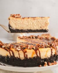 A slice of Turtle cheesecake being lifted from the rest of the cheesecake on a plate below.