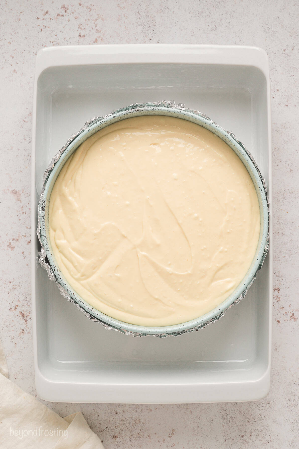 A springform pan filled with caramel cheesecake batter placed inside a water bath.