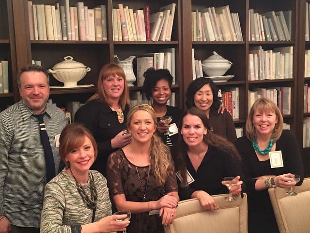 A group of food bloggers posing in front of a bookcase of dishes and books