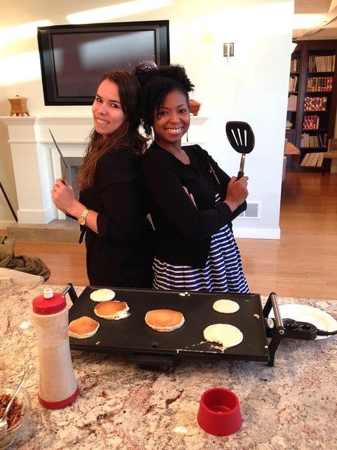 Two food bloggers standing back-to-back in front of an electric griddle cooking pancakes