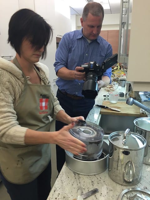 A woman preparing a cake while a videographer records her work