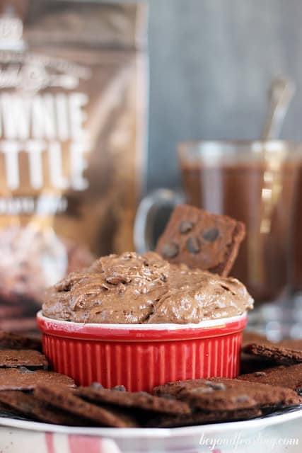 Side view of a bowl of Brownie Brittle Hot Chocolate Dip surrounded by pieces of Brownie Brittle on a plate