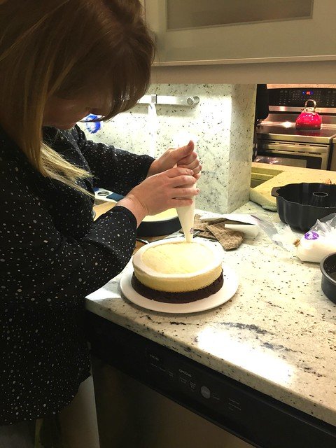 A woman piping frosting onto a layer cake