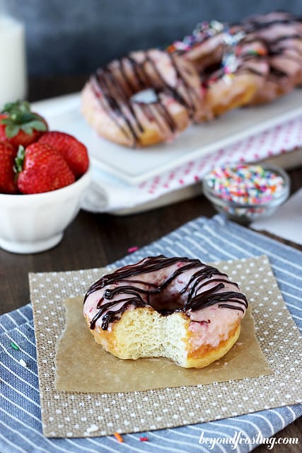 A chocolate covered Strawberry Donut on a napkin with a bite removed