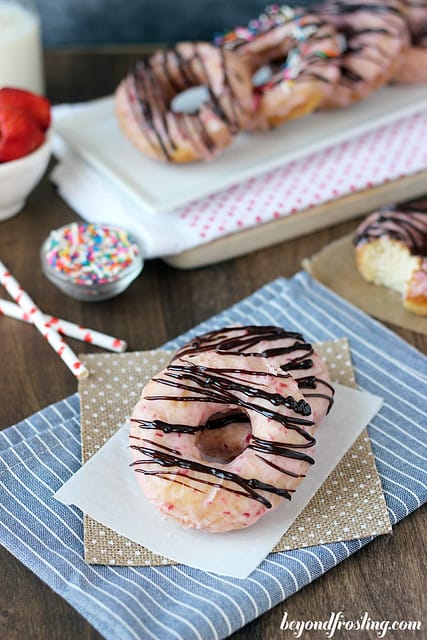 Overhead view of two Chocolate Covered Strawberry Donuts on a napkin with several lined up on a platter