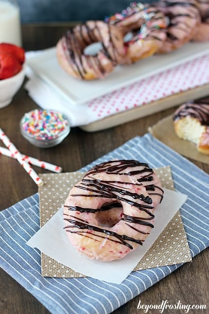 Overhead view of two Chocolate Covered Strawberry Donuts on a napkin with several lined up on a platter