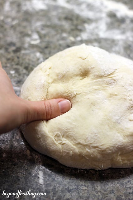 A finger pressing into a ball of donut dough