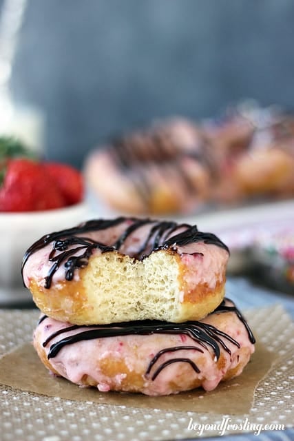 Two chocolate covered strawberry donuts stacked with a bite out of the top one