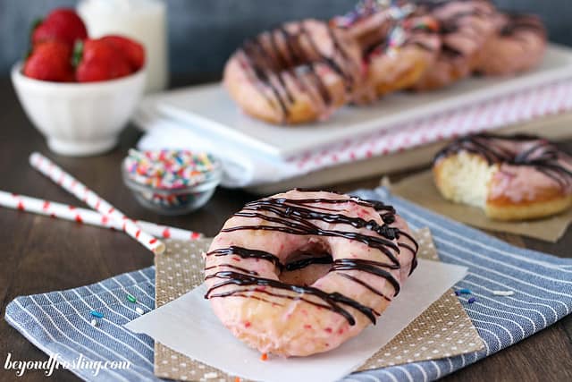 A chocolate covered strawberry donut on a napkin in front of a platter of donuts