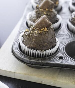 Chocolate cupcakes in a baking pan topped with creamy chocolate butterfinger frosting