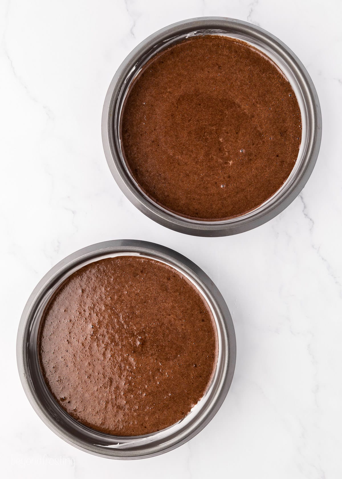 Overhead view of two baked chocolate cakes in round cake pans.