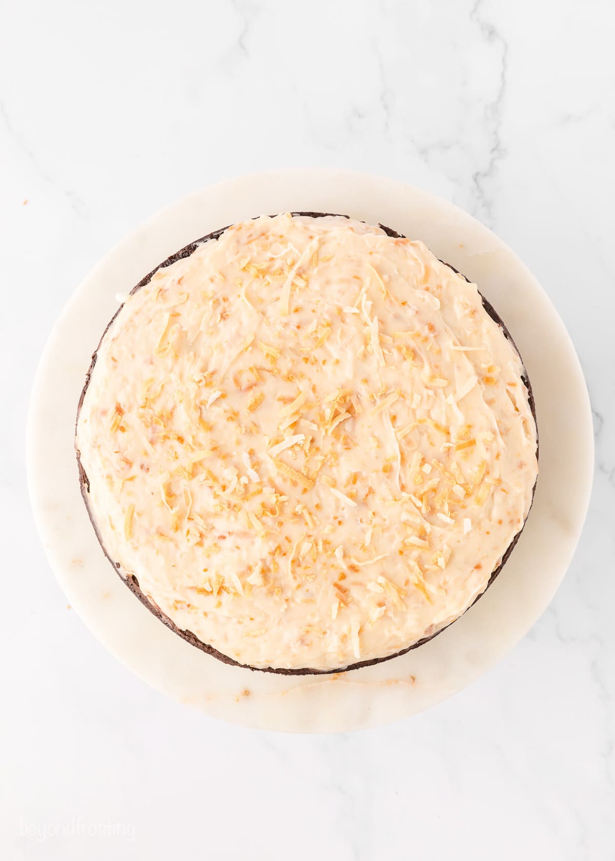 Overhead view of a chocolate cake layer frosted with caramel cream cheese frosting and topped with toasted coconut.