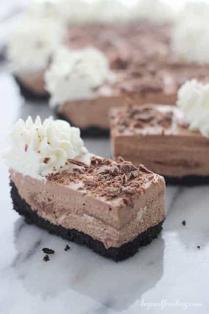 A piece of chocolate mousse tart with whipped cream and chocolate shavings on top plus more pieces in the background