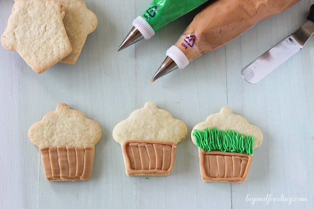 Overhead view of partially decorated flower pot cookies with piping bags of frosting