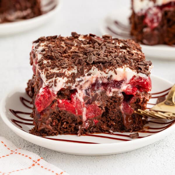 A slice of black forest poke cake next to a fork on a plate, with more cake slices on plates in the background.