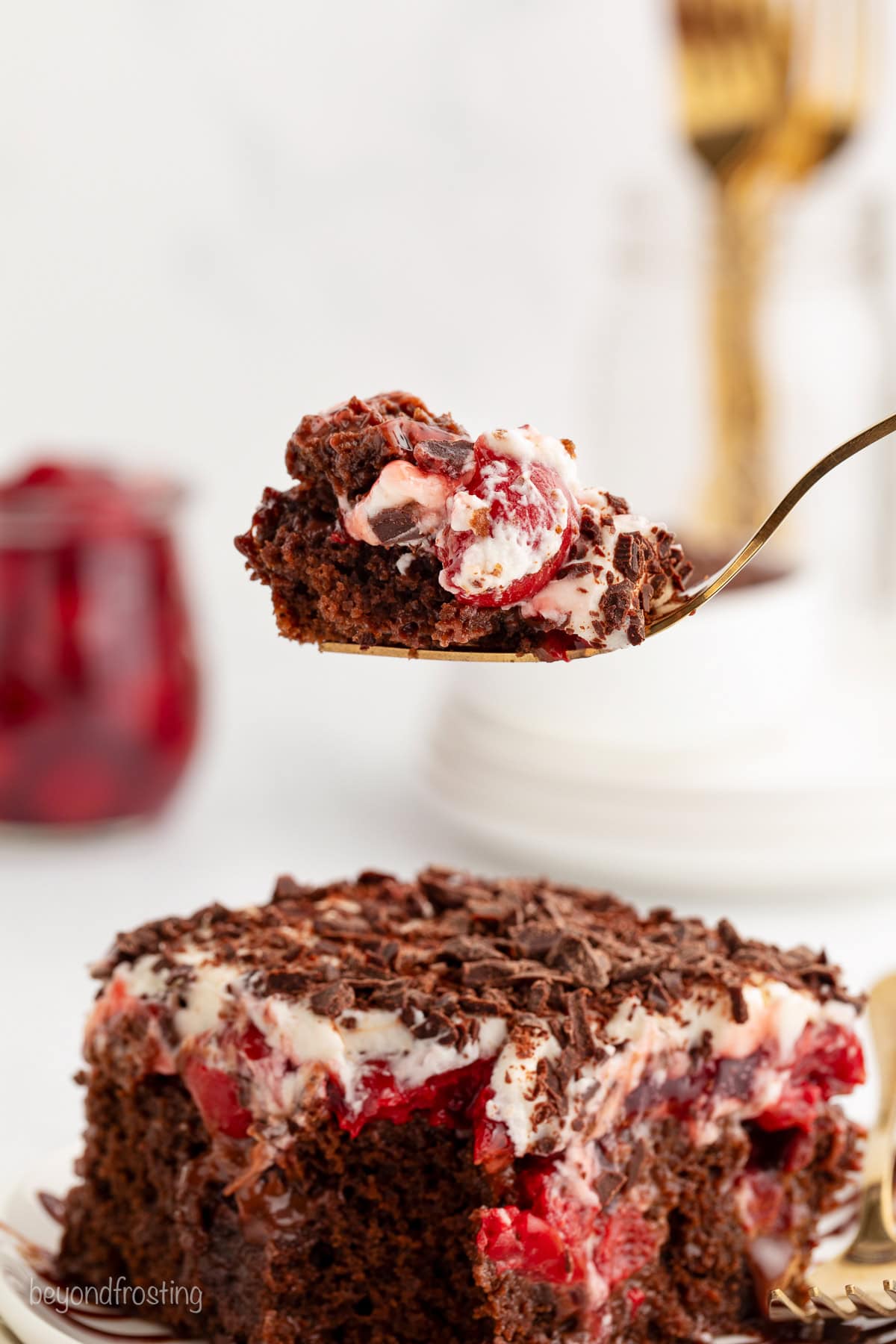 A forkful of cake held over a slice of black forest poke cake.