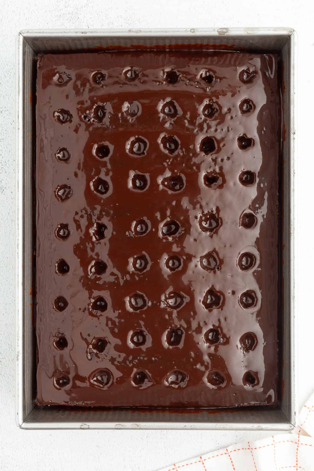 Overhead view of a chocolate poke cake covered with hot fudge sauce in a 9x13-inch pan.