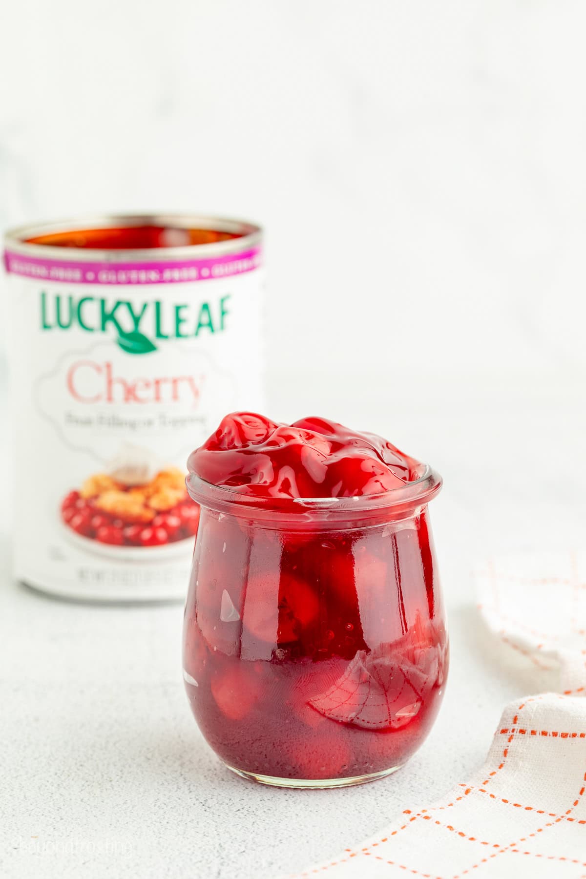 Cherry pie filling in a glass jar with a can of Lucky Leaf pie filling in the background.