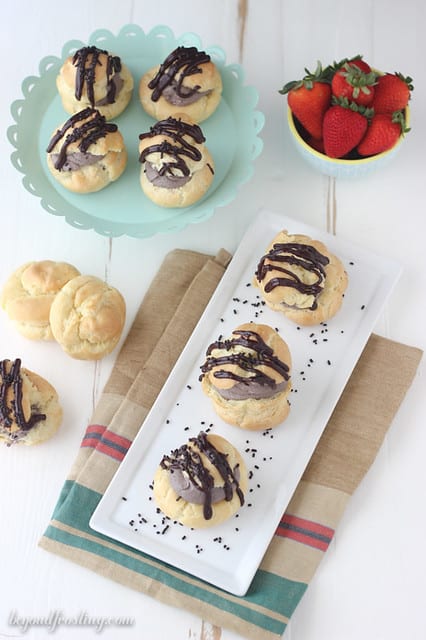 Overhead view of chocolate cream puffs on a plater and a cake stand next to a bowl of strawberries