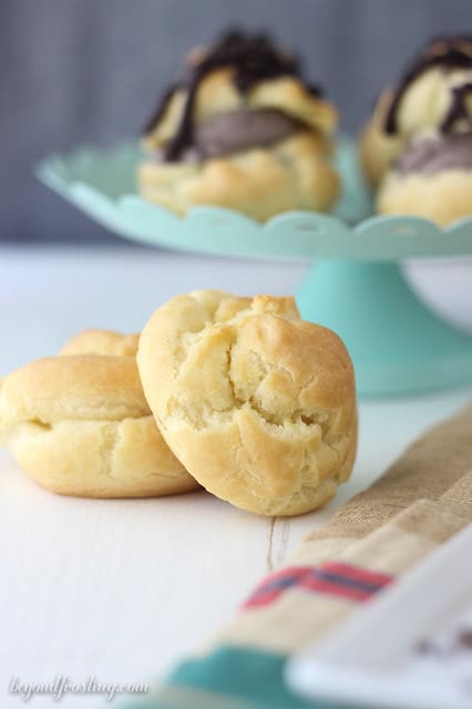 Cream puff shells in front of a cake stand of chocolate cream puffs
