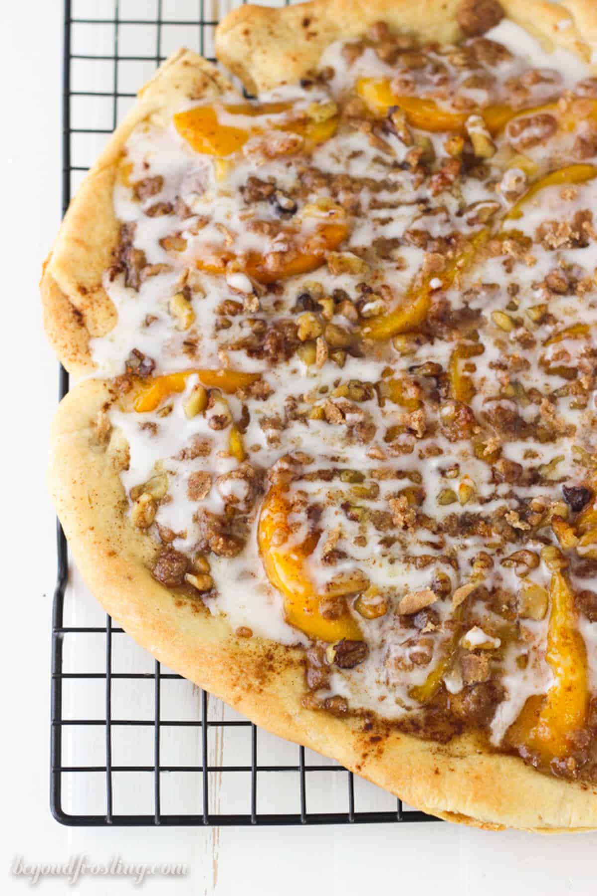 Overhead view of a peach dessert pizza drizzled with glaze on a wire rack.