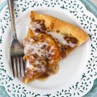 Overhead view of a slice of peach pizza on a plate next to a fork.