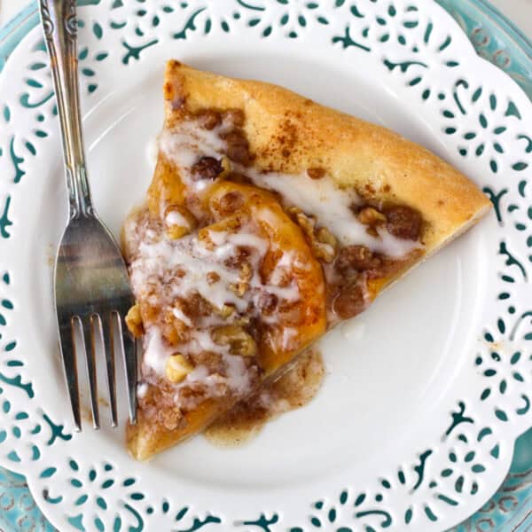 Overhead view of a slice of peach pizza on a plate next to a fork.