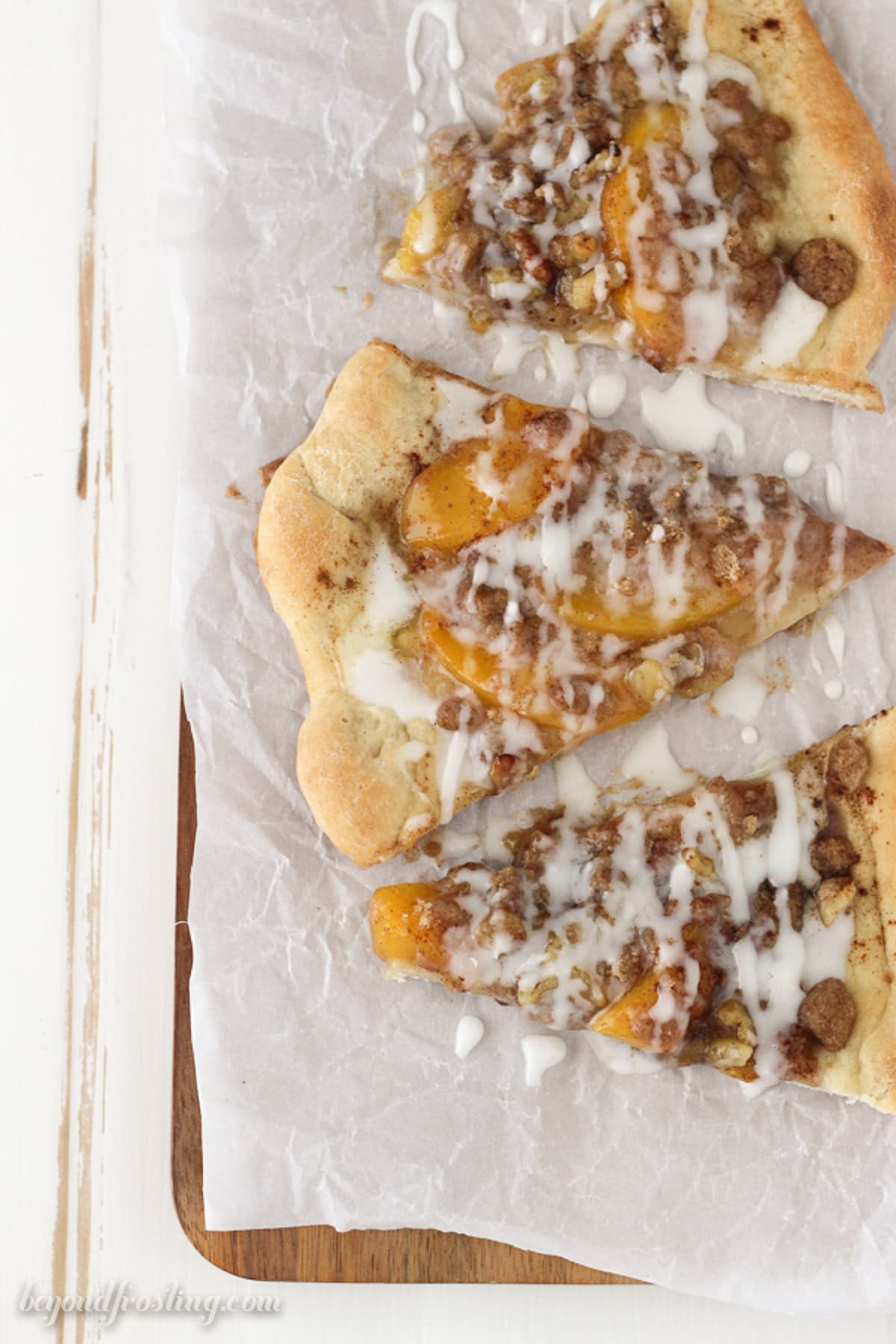 Overhead view of a slice of peach pizza slices on a parchment-lined cutting board.