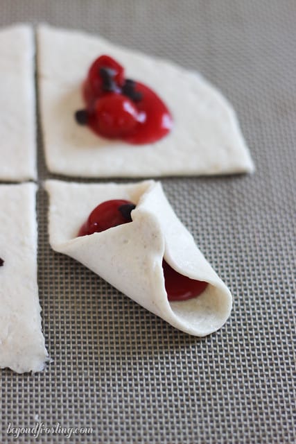 Cherry pie filling being folded into squares of dough